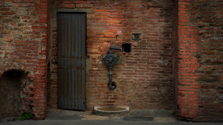 An old door and a water pump in a vintage red brick wall