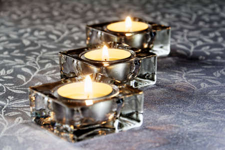 Three lit candles in glass on a white tablecloth at duskの写真素材