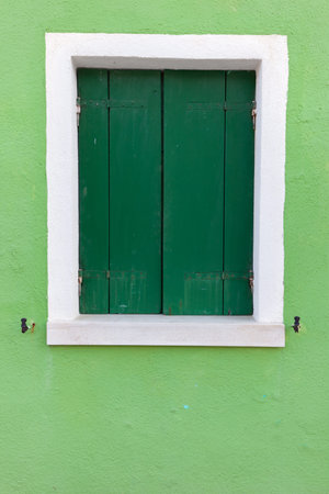 Picturesque old window with dark green shutters on light green wall (Burano island, Venice, Italy)の写真素材