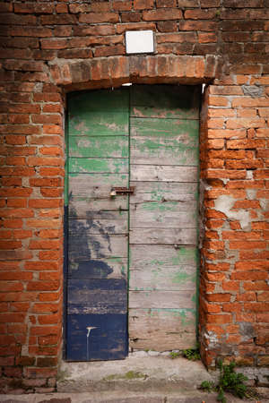 Old wooden door locked with peeling paint in red brick wall (Burano island, Venice , Italy)の写真素材