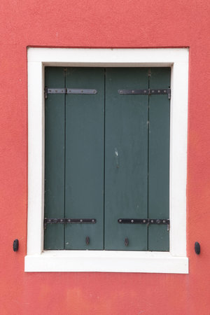 Picturesque old window with dark shutters on red wall (Burano island, Venice, Italy)の写真素材