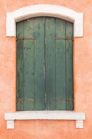Picturesque old window with green shutters on light orange wall (Burano island, Venice, Italy)の写真素材
