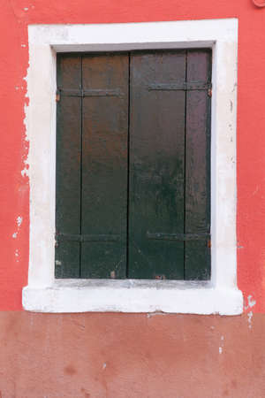 Picturesque old window with dark green shutters on red wall (Burano island, Venice, Italy)の写真素材