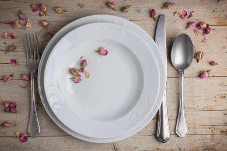Dinner place setting - two plates of white porcelain, fork, spoon and knife on white, old, wooden tableの写真素材