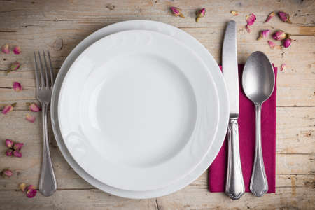 Dinner place setting - two plates of white porcelain, fork, spoon and knife on white, old, wooden tableの写真素材
