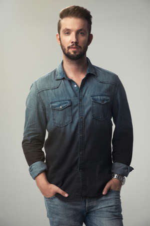 Young strong slim man in jeans shirt posing on gray background.の写真素材