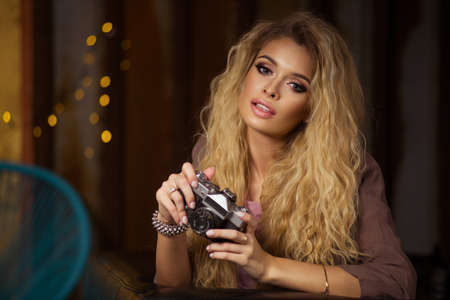 Portrait of a beautiful young blond woman with a camera in home, lifestyleの写真素材