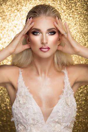 Sensual beautiful blonde woman posing in white dress over gold background. Girl with long curly hair.の写真素材