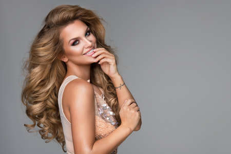 Sensual beautiful blonde woman posing in shining dress. Girl with long curly hair.の写真素材