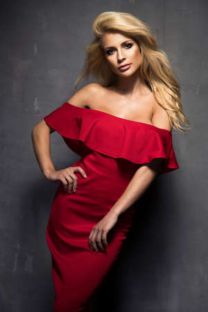Sensual beautiful blonde woman posing in red dress. Girl with long curly hair.の写真素材