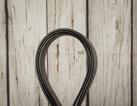 Three stylish dark red leather belts with silver buckles, arranged in a semi-circle on a light brown...