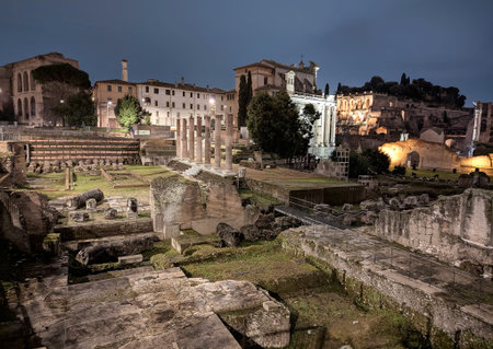 A captivating view of the Roman Forum bathed in the golden light of floodlights at dusk. This iconic...