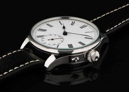 Close-up shot of a vintage-style wristwatch featuring a white dial with Roman numerals, a subdial for seconds, and a black leather strap with white stitching. Displayed on a black background to emphasize its elegance and precision.の写真素材