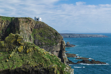Dramatic scenery of the coast consisting of cliffs and a white house. Holyhead Peninsula, Wales, Uk...