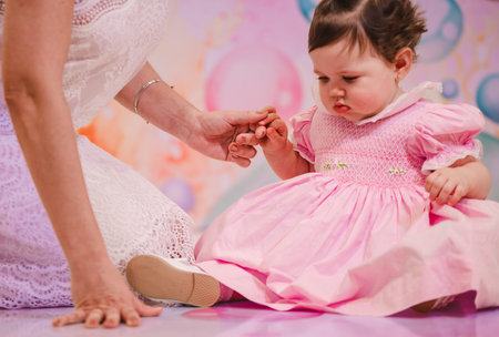 Little girl in a pink dress and her mother hold her hands.の写真素材