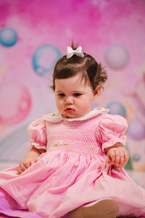 Cute little girl in a pink dress on a pink background.の写真素材