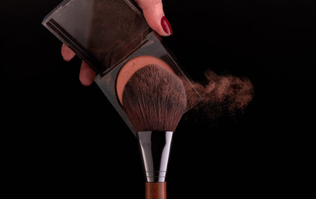 Make-up brush spraying powder on black background