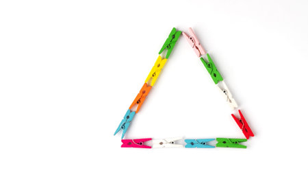Triangle laid out of colored wooden clothespins on white background. Space for text. Top view....