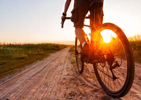 Cyclist on a gravel bike rides along sandy road at sunset. Back view. Active sport concept.の写真素材