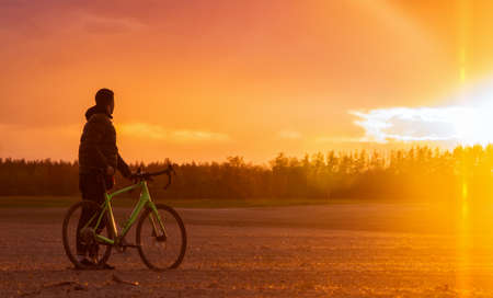 Man with a gravel bike stands in a field on a beautiful sunset background. Beautiful landscape with mountain bicycle.の写真素材