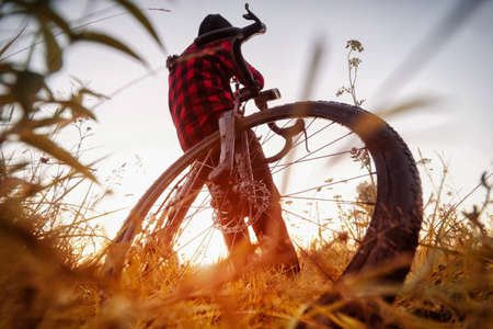 Man with bike in the field. Wide angle view of a cyclist sitting on his bicycle at sunrise in a field with grass. Active lifestyle concept.の写真素材