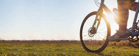 Close-up of a girl on a bicycle riding on green grass against the backdrop of the setting sun. Sports lifestyle, cycling training.の写真素材