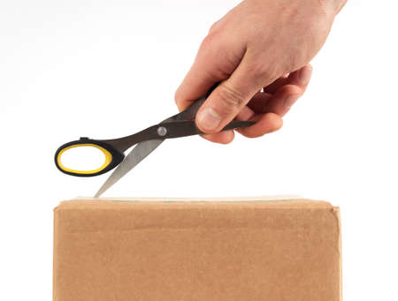 Hand with scissors cuts a cardboard box on white background.の写真素材
