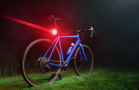 Blue gravel bike with a bright red flashing light on a green lawn in the dark. Alternative to public transport.の写真素材
