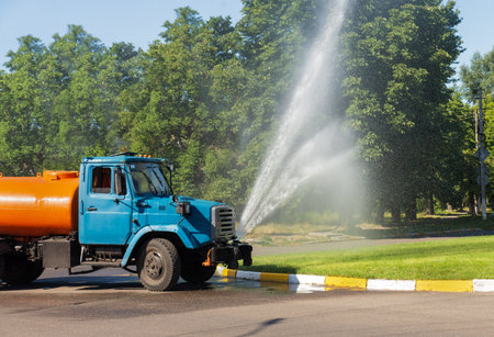 Truck sprinkles water on a green lawn in the city. Urban economy. Improvement of green areas.の写真素材