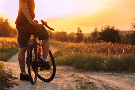 Man with bicycle standing on dusty trail in the field at sunset. Cycling concept.