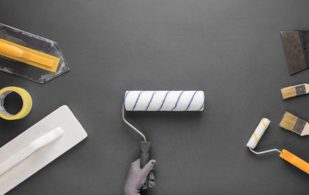 Roller for painting in a gloved hand and other tools for repair on a gray background.の写真素材