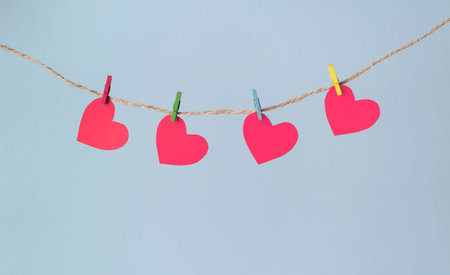 Paper hearts hang on clothespins on a rope on a pastel blue background. Valentine's day concept.