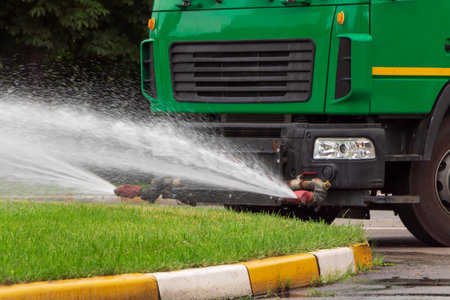 Close up of truck sprinkles water on the green grass. City care services.の写真素材