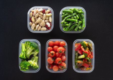 Frozen vegetables in plastic containers on black background.