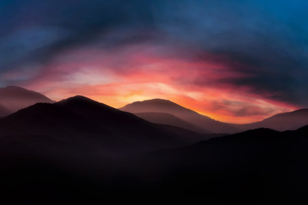 Mountain landscape at sunrise. Dramatic cloudy sunrise sky over mountain tops in morning fog