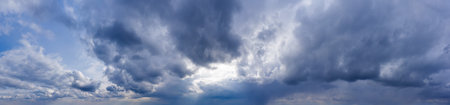 Dark clouds against a blue sky with sunbeams shining through. Sky panorama.