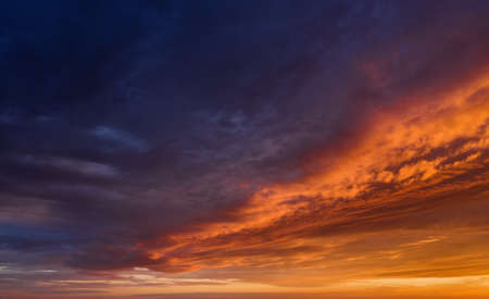Vibrant sunset sky background with dark clouds illuminated by orange sunlight.の写真素材