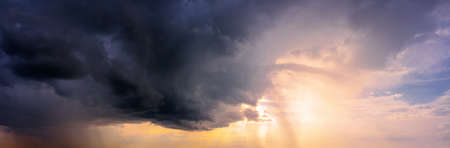 Dramatic sky panorama with bright sun shining through the dark rainy clouds. Natural background.の写真素材