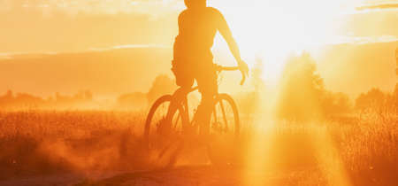 Silhouette of a professional cyclist riding on a countryside trail with dramatic sunset background. panoramic view. Sport an active lifestyle.の写真素材