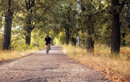 Cyclist in motion. Active man on a bicycle rides on a country road in the woods on a summer evening.の写真素材