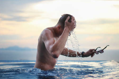 Young man in the infinity pool on a background of beautiful sunset. Tourism and vacation concept.の写真素材