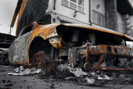 A burnt-out destroyed car near a civilian building. The result of mortar shelling during the Russian-Ukrainian war.の写真素材