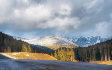 Beautiful winter landscape with mountains covered in snow, trees, road and cloudy sky at sunny day.の写真素材