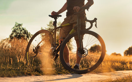 Cyclist with bicycle on a dirt trail at the sunset in the field. Beautiful evening landscape with a bicycle. Active lifestyle concept.の写真素材
