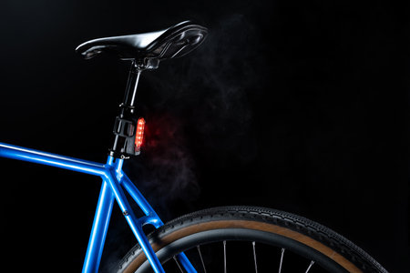 Blue gravel bike with illumination of red rear flasher, cycling safety and sleek design against dark background with white smokeの写真素材