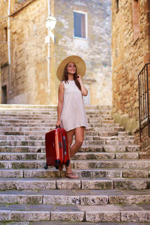 Young girl with suitcase on the stairs of the old townの写真素材