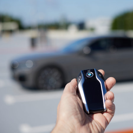 A man's hand holding a remote control for a BMW car against the background of a silhouette of a BMW...