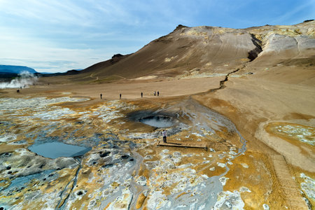 Hverir, Iceland. Tourists walk amidst unique geothermal features, including bubbling mud pits and vibrant mineral patches at a natural site in Iceland.の写真素材