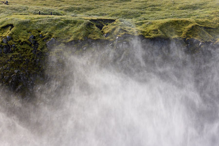 Water flows dramatically over rocky cliffs, creating mist in a lush, green environment.の写真素材