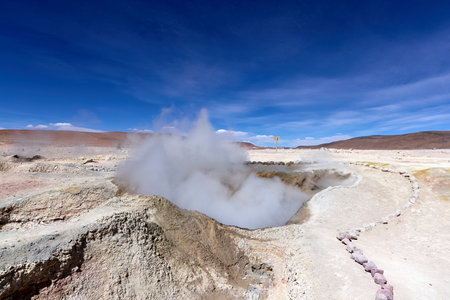 Active geothermal field with steam vents and yellow sulfur deposits in the Avaroa National Park. Natural hot springs and geysers under vibrant blue sky in high-altitude volcanic terrain.の写真素材
